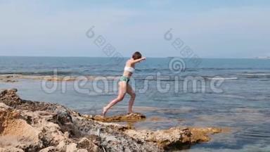 年轻的白种人黑发女人，穿着<strong>泳装</strong>，腿上长着蜂窝织体，沿着岩石海滩漫步